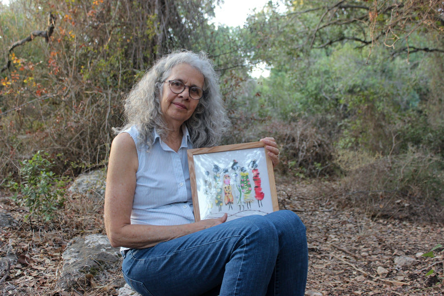 Artist Shirley Regev holding a framed FloraFusion botanical art print in nature