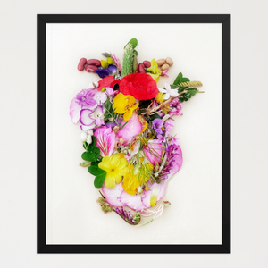 Heart shape built from layered petals, blossoms, seeds, and greenery in pinks, yellows, reds, and purples. Botanical wall art by FloraFusion.